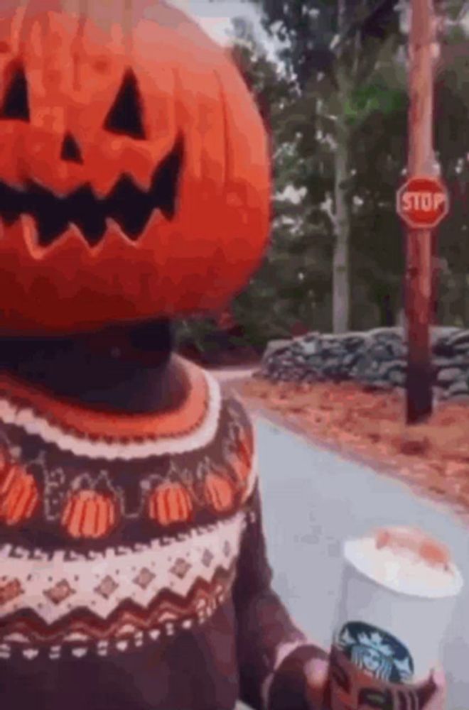 a person with a pumpkin on their head holding a cup of coffee .