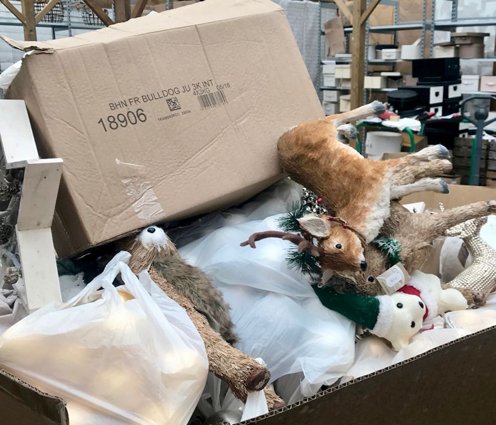 In a dump behind a supermarket a heap of empty cardboard boxes and Christmas decorations like fake stuffed animals, a snowman and Christmas balls. 