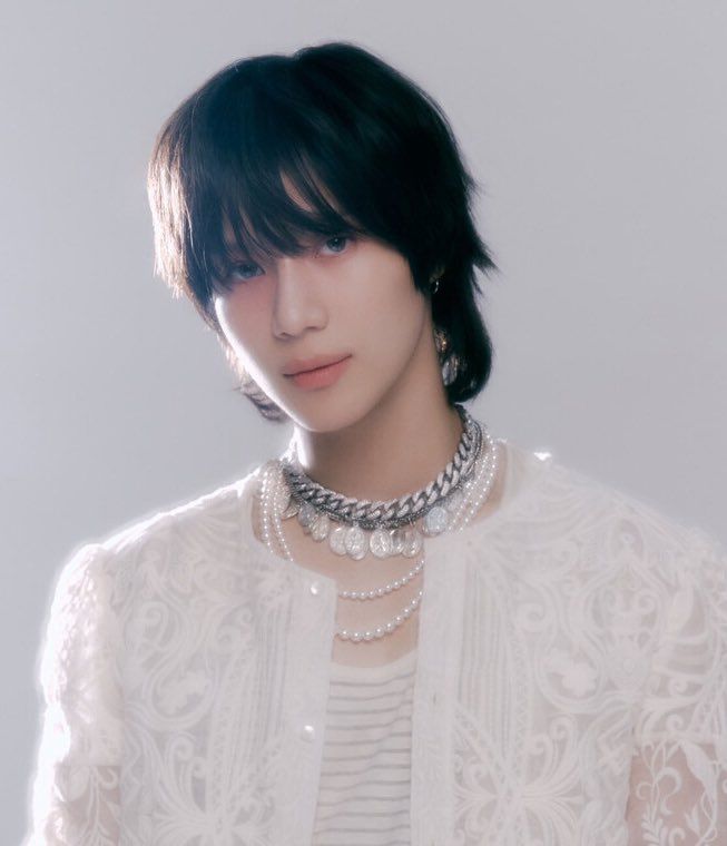 the light and focus of the pic give him an etheral look, the very light make up and style and fluffy hair underscore it. he is wearing a very heavy silver necklace with coins and two pear necklaces. He has a striped shirt on with a white lace jacket.