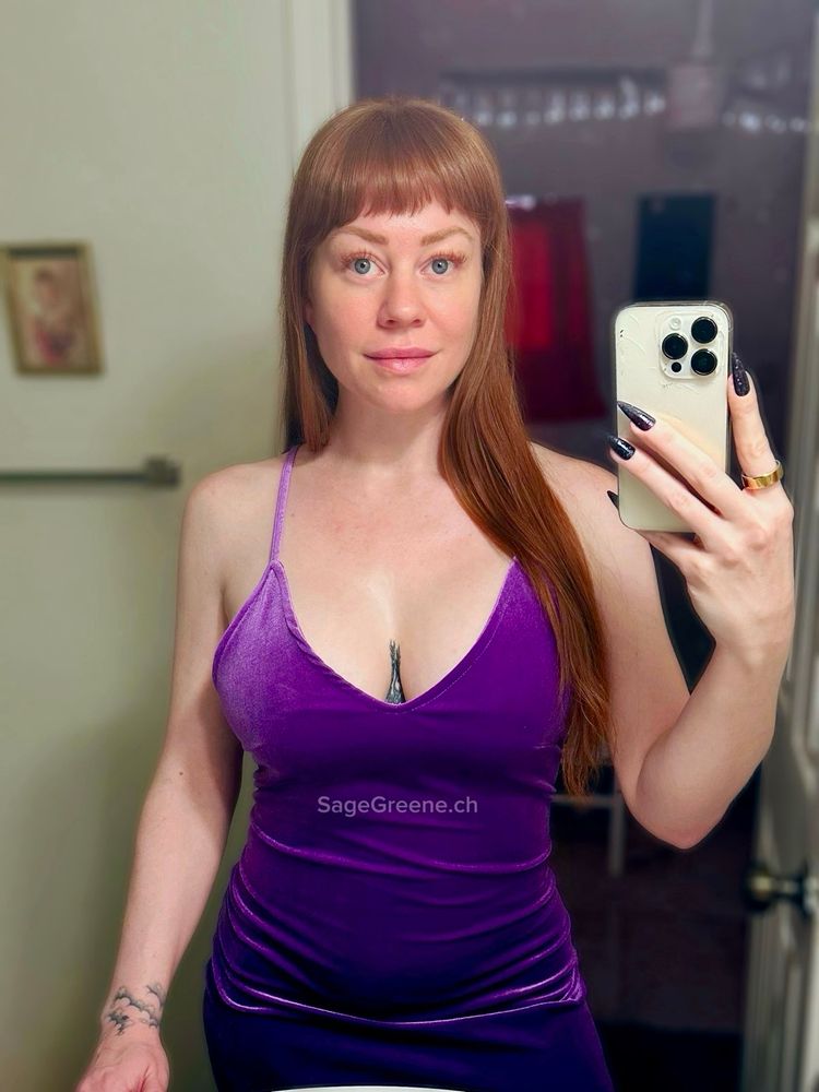 Redhead woman taking mirror selfie wearing purple velvet dress.
