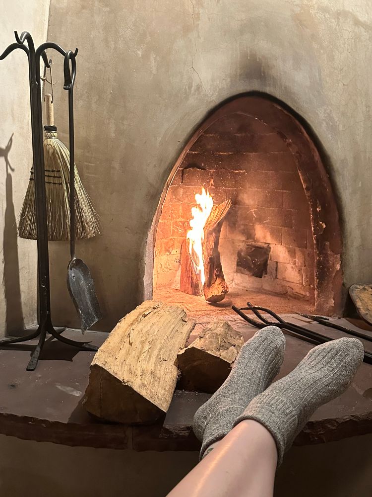 Stockinged feet before a fire in a fireplace.