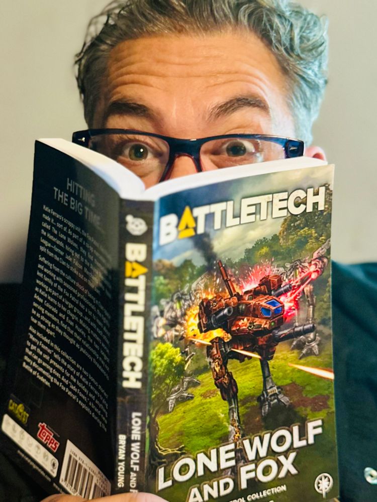 The author excitedly devouring his own work like some sort of weirdo. In his hands is a copy of BattleTech: Lone Wolf and Fox, his eyes peek out from behind it like a creeper.