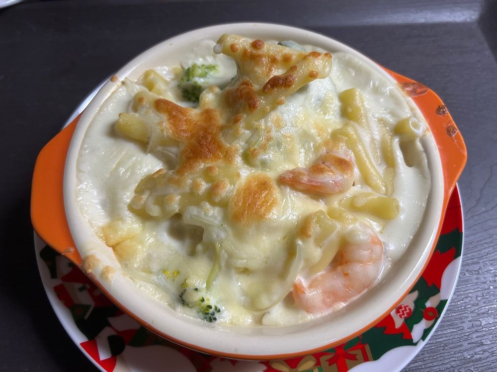 皿の上にグラタンが置かれている。ホワイトソースに大ぶりのエビとブロッコリーがいくつか入っているマカロニグラタン。チーズの焼き目がついている。