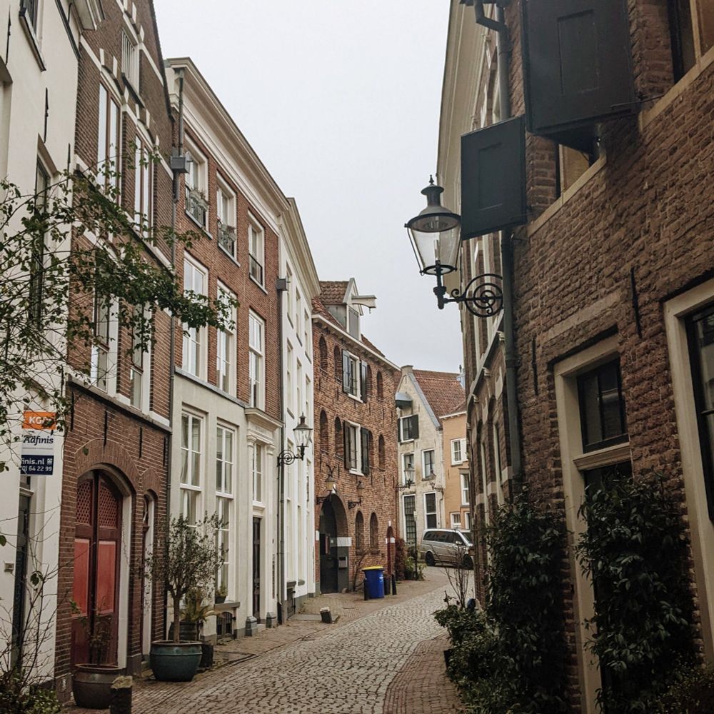 Photo depicting a narrow, cobbled street framed with red brick and white plaster buildings in Deventer, Netherlands.