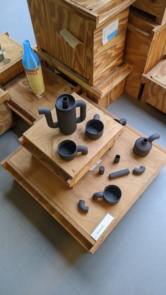 Multiple wooden crates supporting various pieces of a dark grey tea set.