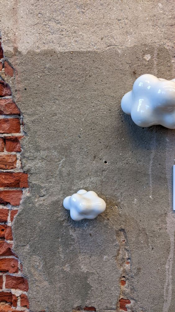 A brick and plaster wall with two white ceramic cloud sculptures mounted on it.