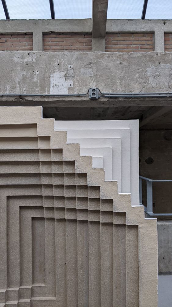 A geometric grey and white ceramic sculpture featuring intersecting ridges and corners.