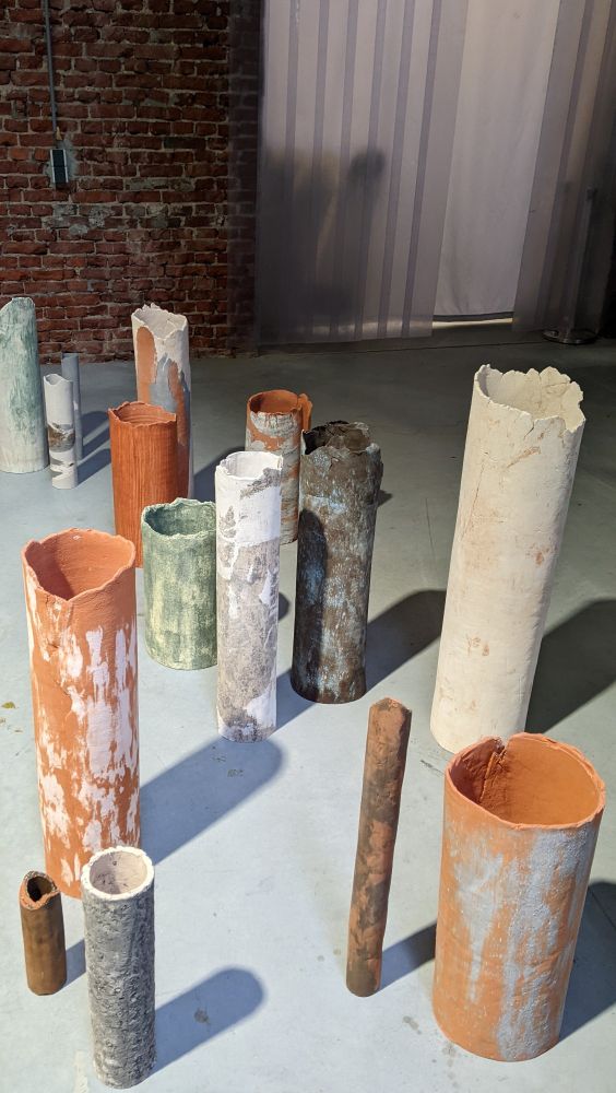 Multiple multicoloured ceramic cylinders of varying heights standing on a concrete floor.
