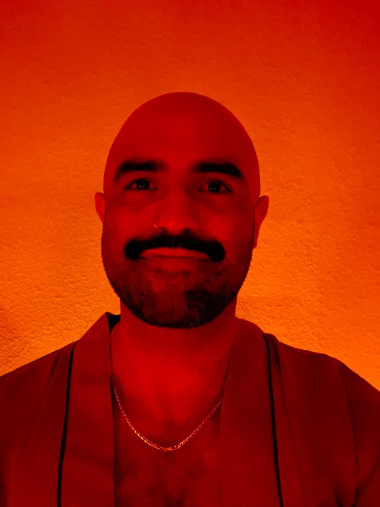 Moustachioed Salvadoran wearing a bath robe, in a dimly lit spa treatment room. 