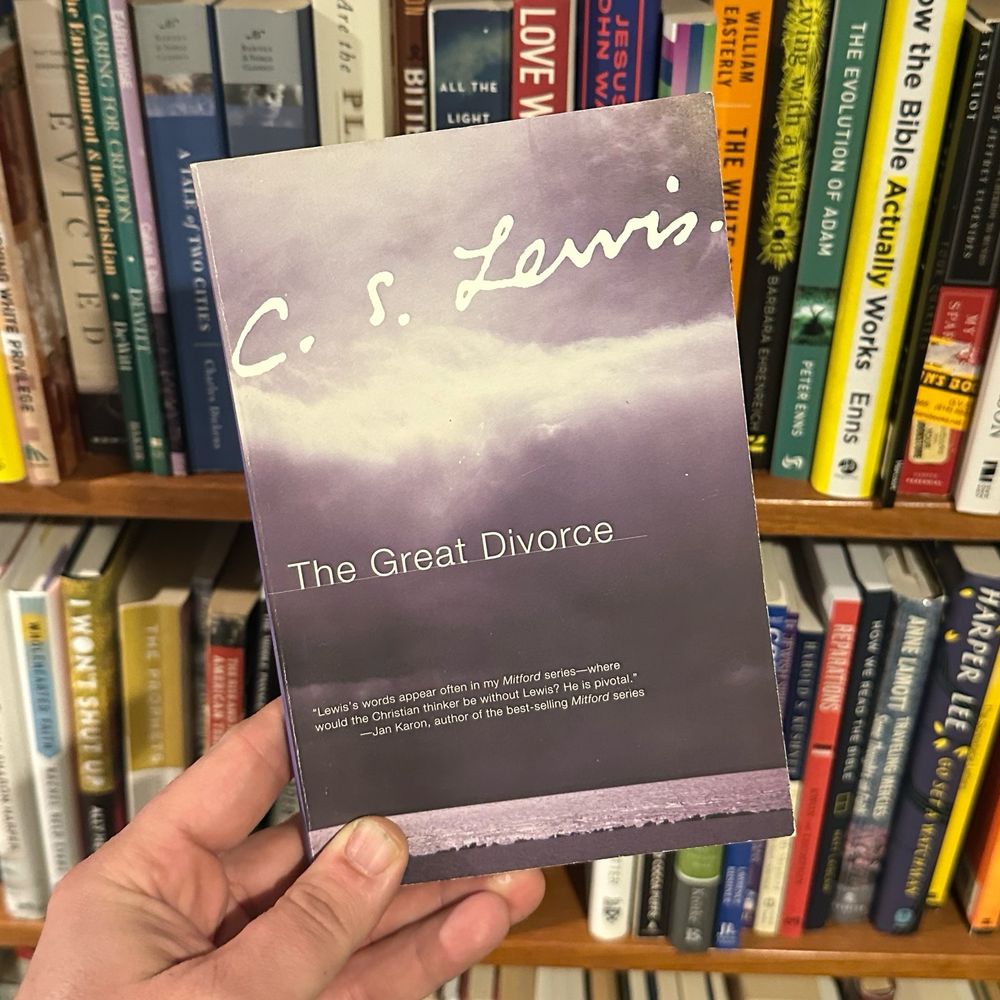 Copy of a paperback edition of The Great Divorce by C.S. Lewis held in a hand infront of a bookshelf 