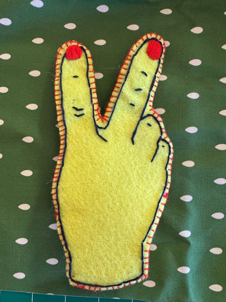 Embroidered felt — the outside of a hand making the bunny ears (peace) sign