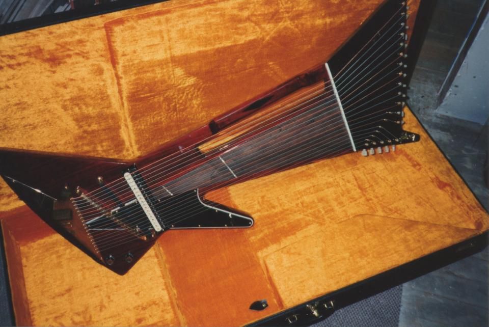 I don't know how I'm going to top this Explorer-shaped harp that Gibson made in 1993. It's got 18 strings, an oversized Explorer body, a massive unfretted neck with a gap in the middle to give you a place to grab onto it, and a gigantic 13/5 split headstock. The top 13 tuners are vertical, and the bottom 5 face the ground, making for some weird string angles. It's got a massive zebra-stripe humbucker, one volume, and one tone control. It's even got its own hardshell case with orange fuzz on the inside!