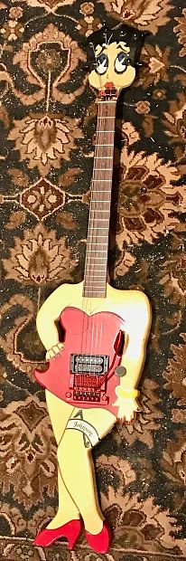 The first post I made that got lots of attention was when I posted guitars that Johnson made that looked like Gumby (guitar) and Pokey (bass). Here's another one they made.

If you look at the hardware on this guitar, it's a fairly standard super-Strat: one humbucker, volume knob, locking trem. No big deal, right? Well, instead of having a normal Strat body, this body's shaped and painted like Betty Boop. Her right hand's on her hip, and her left knee is popped out. Her head is the headstock of the guitar, and the tuners are arranged around the edge of her hair. The locking nut looks like a necklace. She's wearing a garter belt that says "Johnson" on it. The pickup and bridge are in her stomach area, and the volume knob is on her left arm.