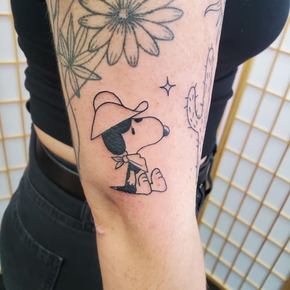 Cowboy snoopy tattooed on the lower upper arm just black outline 