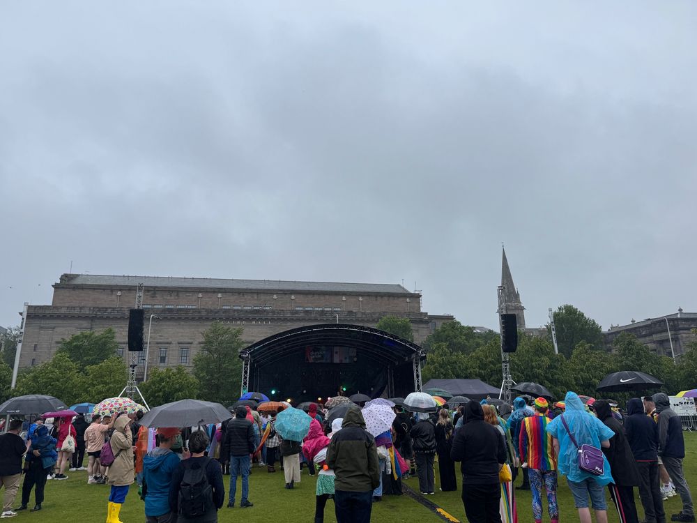 Dundee Pride attendees under umbrellas facing the stage while a Drag act performs.