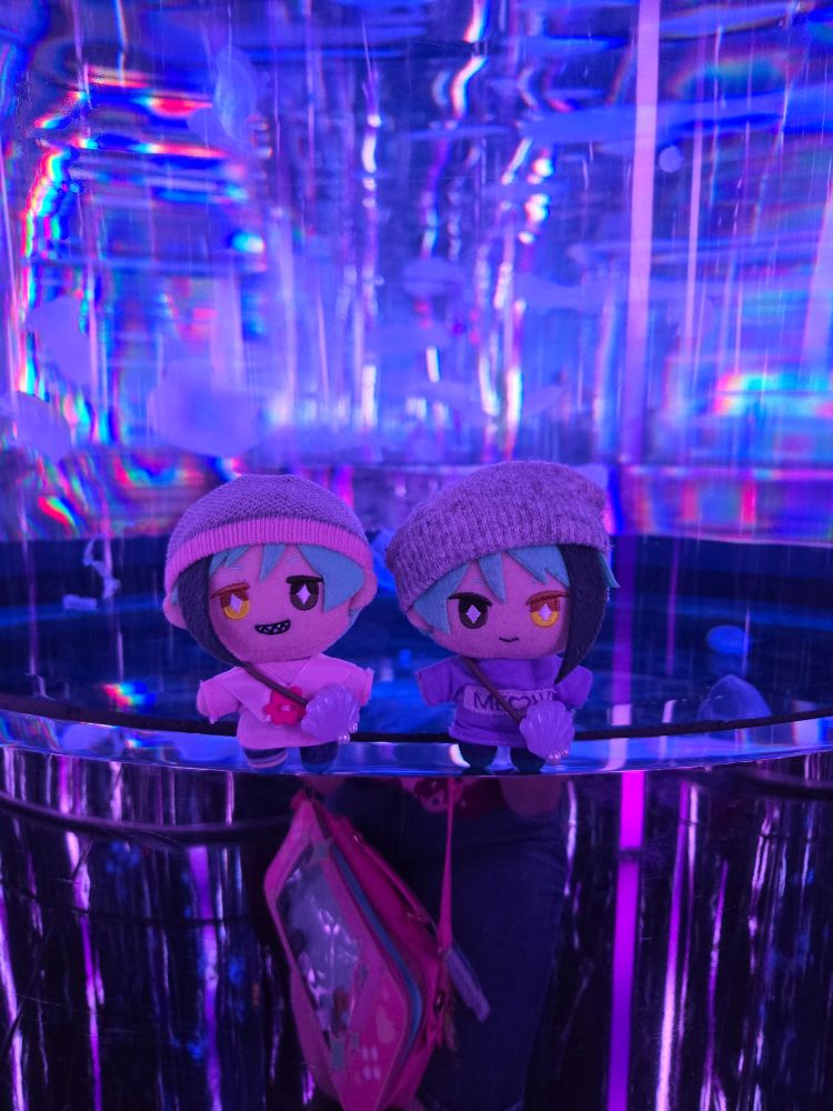 A Jade Leech nui and a Floyd Leech nui  standing in front of a tank of jellyfish. The room is lit pink, purple, and blue