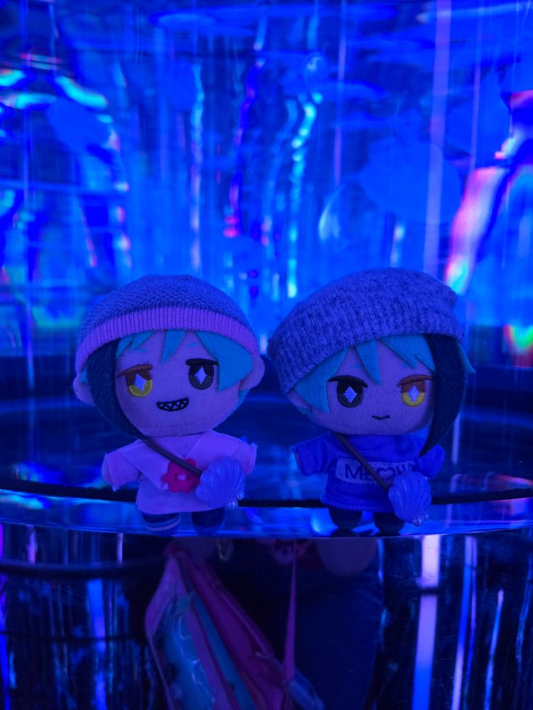 A Jade Leech nui and a Floyd Leech nui  standing in front of a tank of jellyfish. The room is lit a deep blue color with a little pink