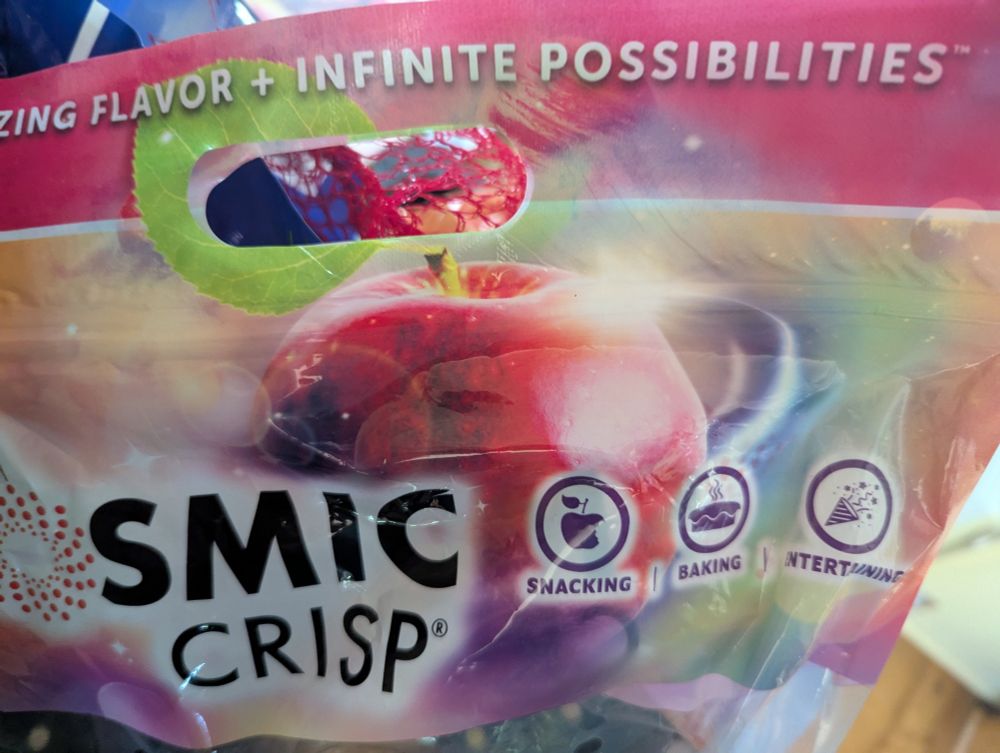 A colorful bag of Cosmic Crisp apples, with the tagline at the top that says "amazing flavor + infinite possibilities". The bag features a big painterly image of an apple with three icons that mention snacking, baking, and entertainment.