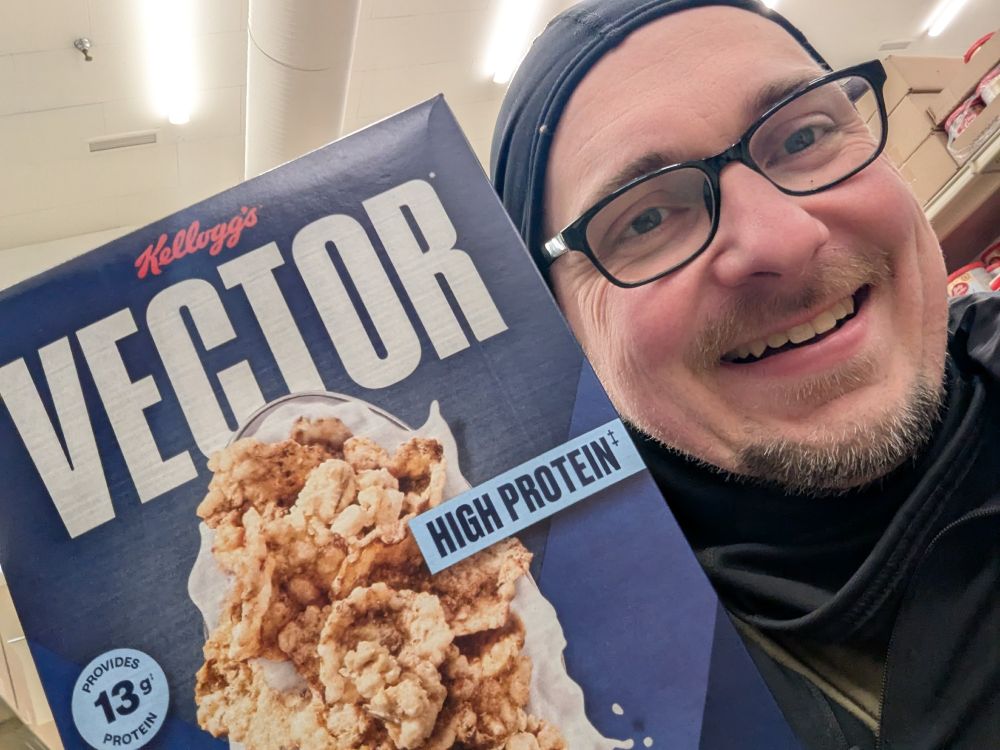 a blue box of Kellogg's VECTOR cereal, showcasing the texture of the flakes and its 13g of protein per serving. The words "HIGH PROTEIN" appear on the box. A man with glasses stands beside the box.