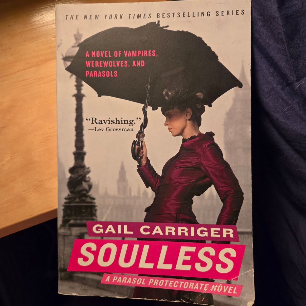 Cover of Gail Carriger's Soulless shows a white woman in a dark magenta dress of approximately Victorian design. She is holding a black parasol with a steam punk style. The tag line says, "A novel ox vampires, werewolves, and parasols."