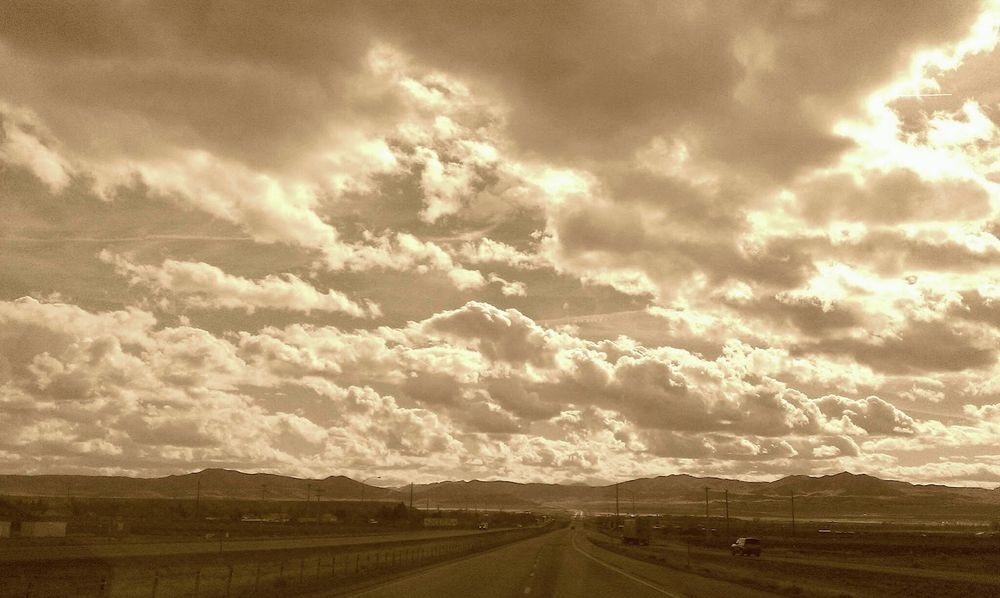 Monochrome shot looking down the highway out west with mountains in the distance and a big sky full of clouds