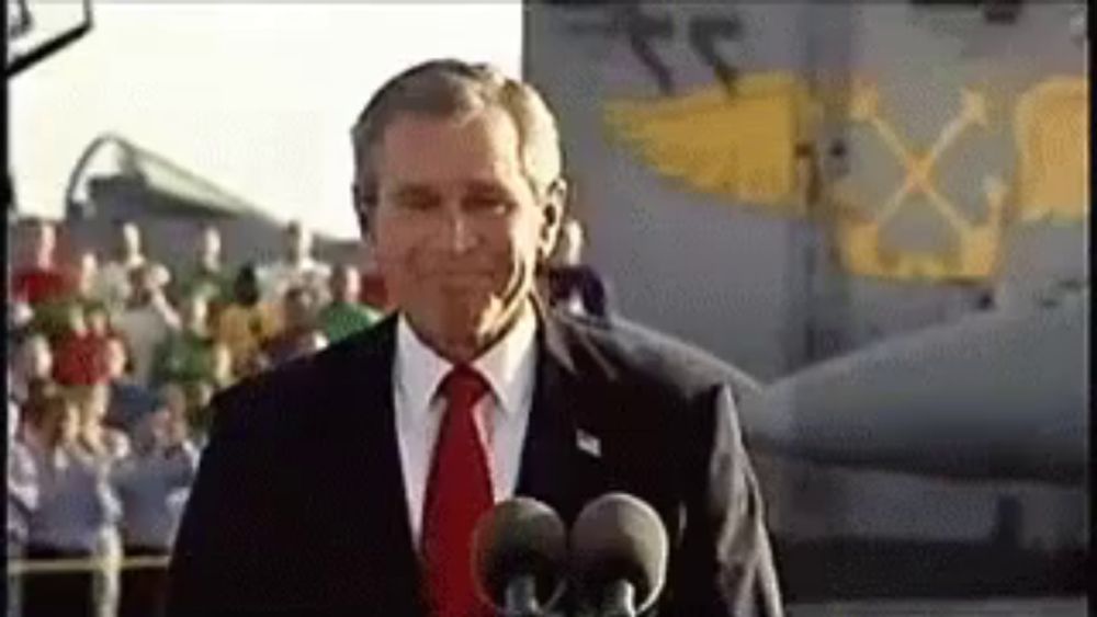 a man in a suit and tie is standing in front of two microphones in front of a plane .