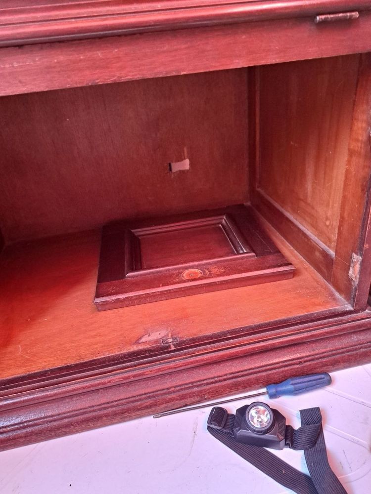 a close up picture of the bottom storage of a wooden cabinet, with its doors removed and one of them resting inside. at the bottom right of the picture, a headlight and a screwdriver rest close to the cabinet