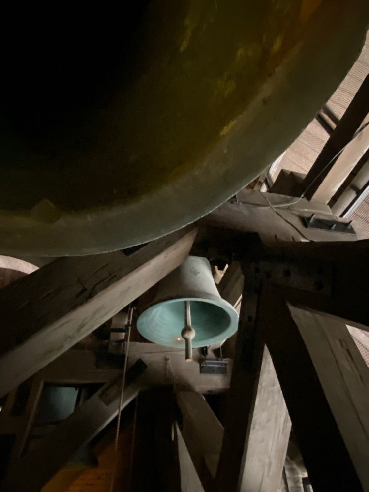 A bell tucked into the shadowed corner of a wooden belfry 
