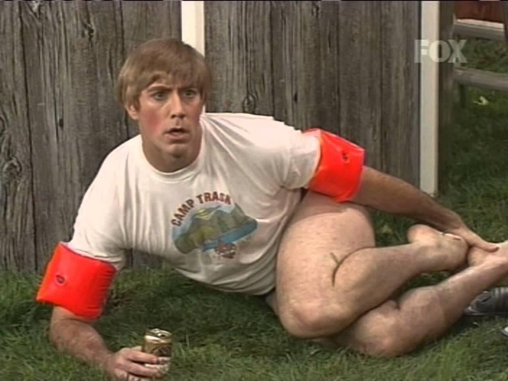 Stewart from Mad TV on the ground wearing pool floating and a Tshirt probably saying "noooooo, stop it"