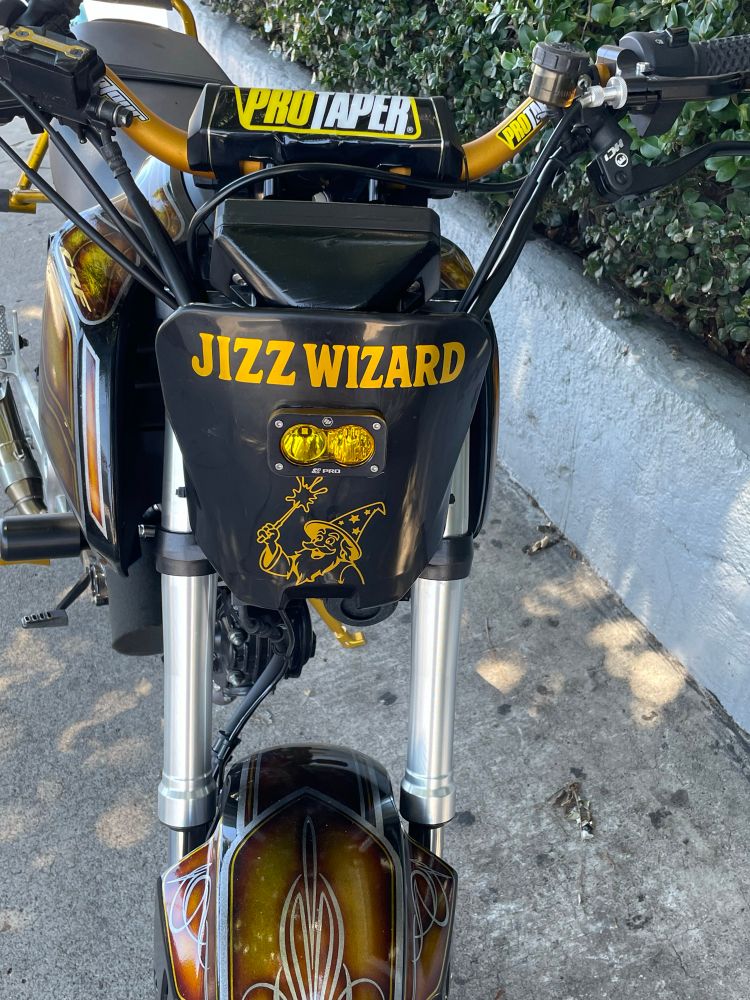 Photo of a black and gold motorcycle with an ornate drawing of a wizard on the front that says JIZZ WIZARD 