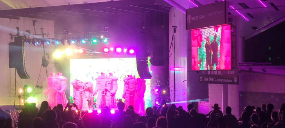 A brightly lit concert with inflatable pink robots on stage. 