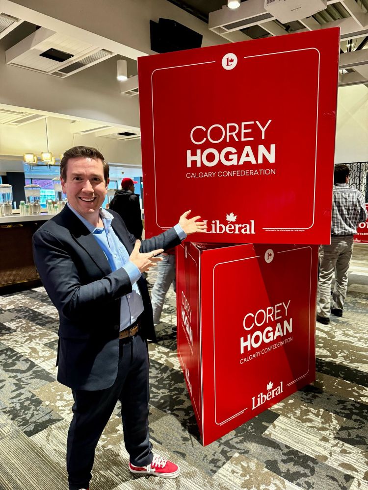Corey Hogan in Liberal red sneakers in front of a tower of his campaign signs.