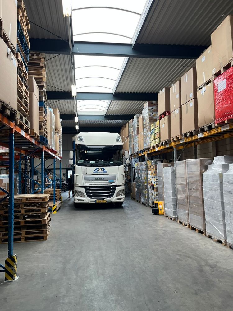A truck inside a large warehouse, pulled up between the shelves.