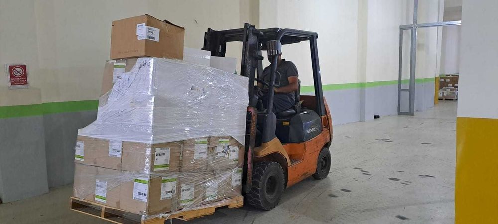 A person operates a forklift carrying a large pallet of boxes.