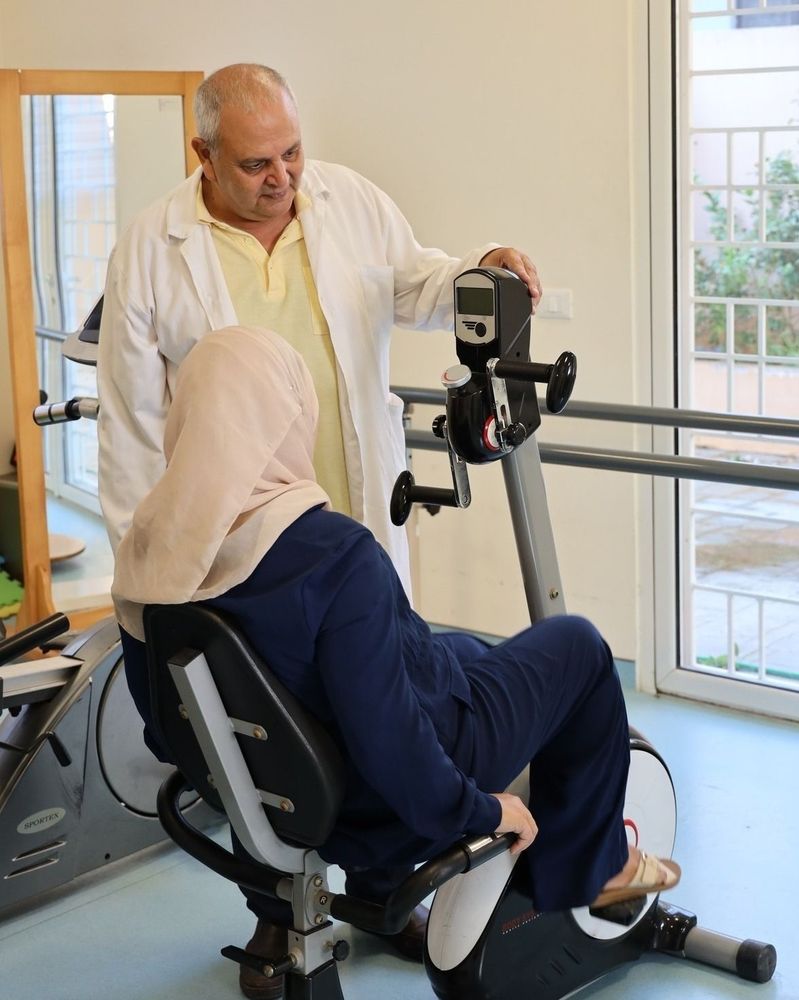 A woman is sitting on a physical therapy exercise chair. A male doctor is standing next to her.