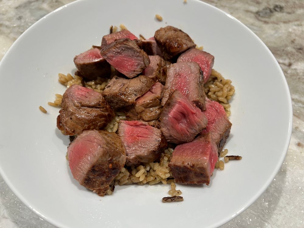 A bowl of brown and wild rice with sliced steak on top of it. The steak was juicy, tender, decently seasoned despite only having salt and pepper to season it with and this being the second time ever the chef had made steak.
