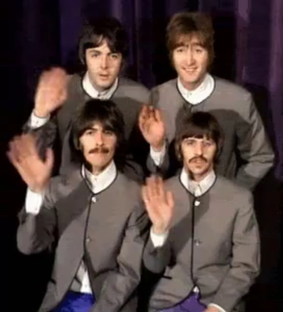 the beatles are posing for a picture while waving their hands .