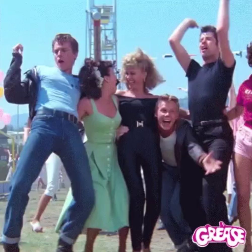 a group of people are dancing in front of a grease sign