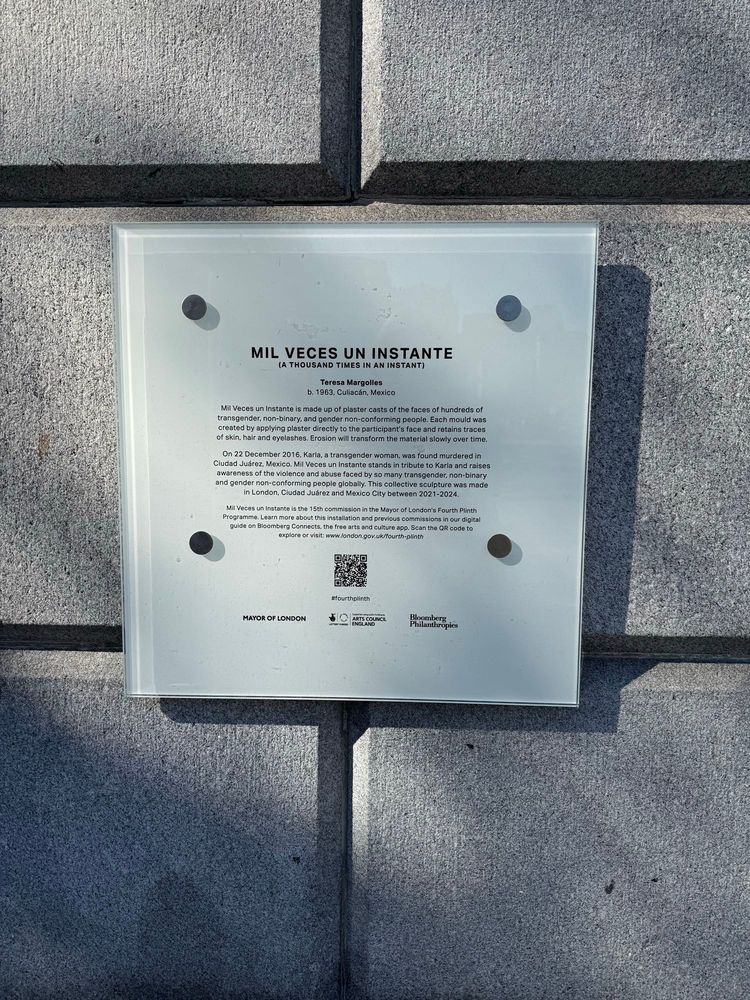 A plaque for the monument that reads (note this is long) "MIL VECES UN INSTANTE
(A THOUSAND TIMES IN AN INSTANT)
Teresa Margolles
b. 1963, Culiacán, Mexico
Mil Veces un Instante is made up of plaster casts of the faces of hundreds of transgender, non-binary, and gender non-conforming people. Each mould was created by applying plaster directly to the participant's face and retains traces of skin, hair and eyelashes. Erosion will transform the material slowly over time.
On 22 December 2016, Karla, a transgender woman, was found murdered in Ciudad Juárez, Mexico. Mil Veces un Instante stands in tribute to Karla and raises awareness of the violence and abuse faced by so many transgender, non-binary and gender non-conforming people globally. This collective sculpture was made in London, Ciudad Juárez and Mexico City between 2021-2024.
Mil Veces un Instante is the 15th commission in the Mayor of London's Fourth Plinth Programme. Learn more about this installation and previous commissions in our digital guide on Bloomberg Connects, the free arts and culture app."