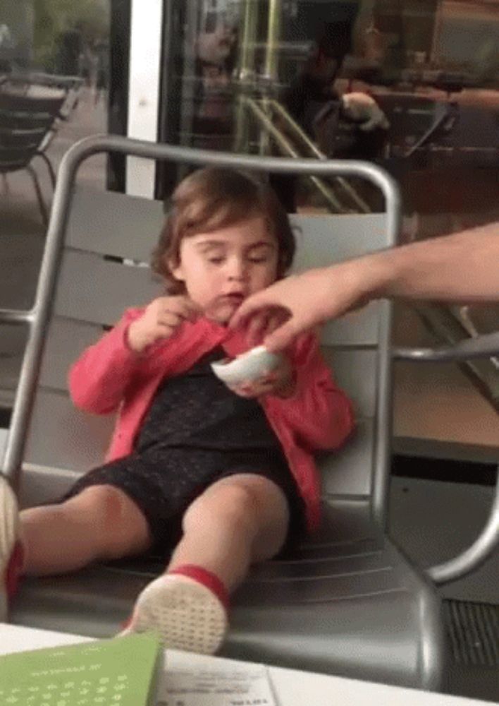 a little girl is sitting in a chair eating a bowl of food