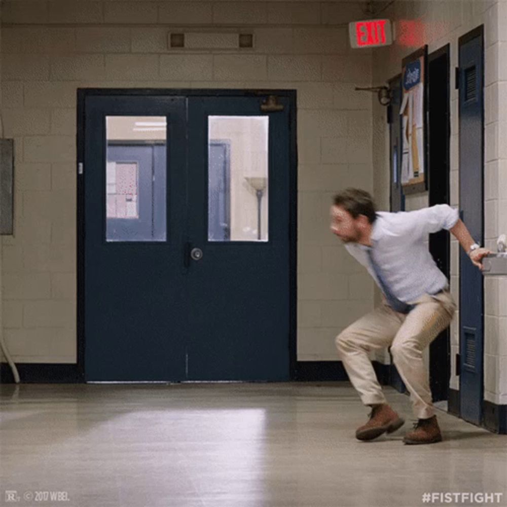 a man is squatting in a hallway with an exit sign above him