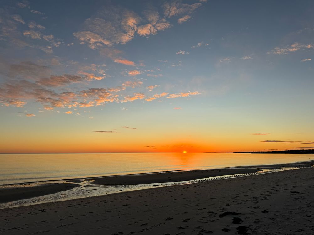 Sun setting into the ocean with beach in foreground 
