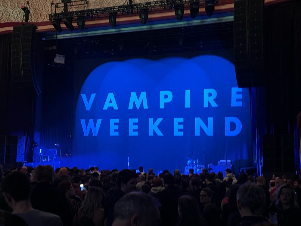 A stage with a black backdrop that says “Vampire Weekend” 