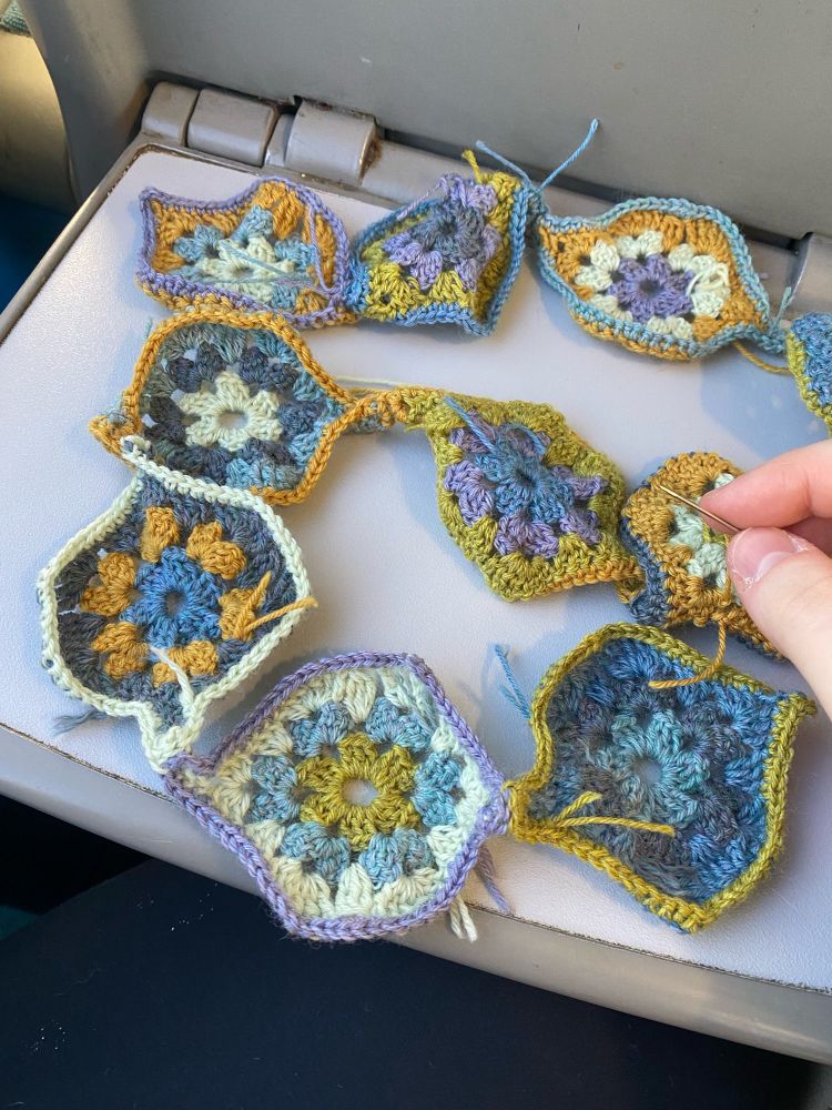 a string of 10 crocheted double S-curved motifs. Each motif has four random colors using a palette of 3 different blues, 2 greens, yellow, and purple 4-ply yarn.