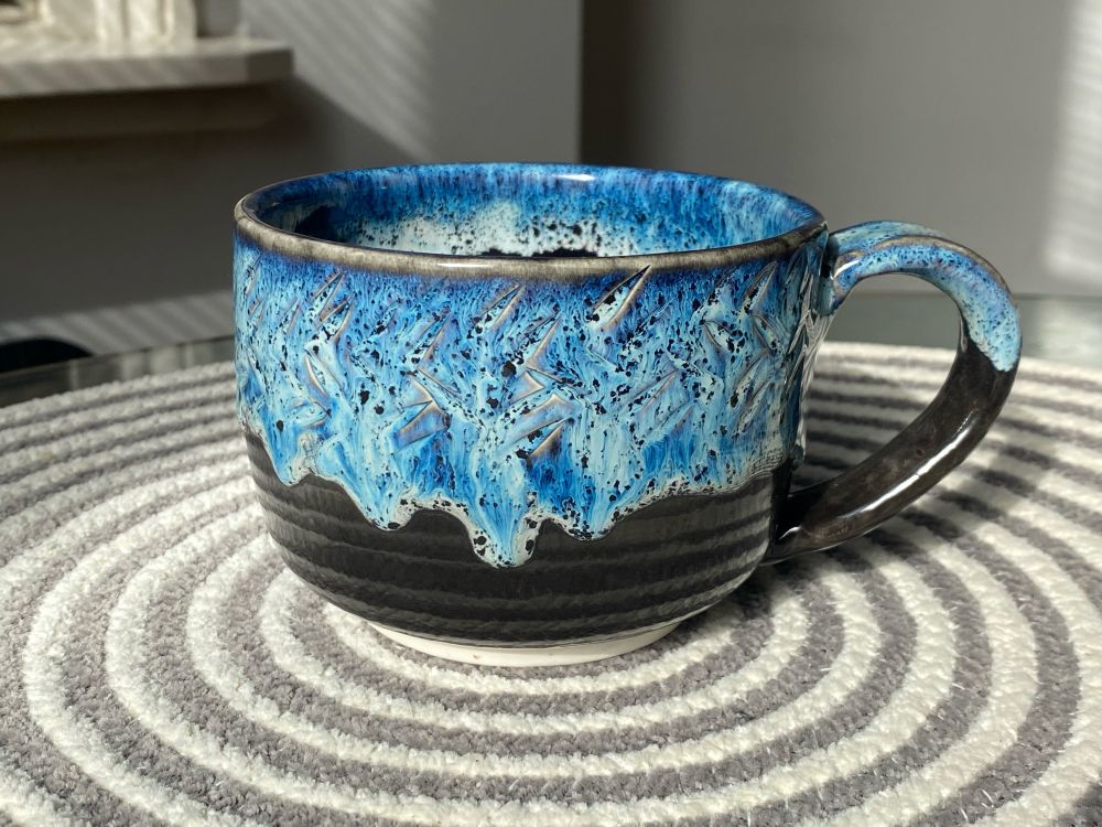 coffee mug with a black base and thick blue glaze dripping down from the top