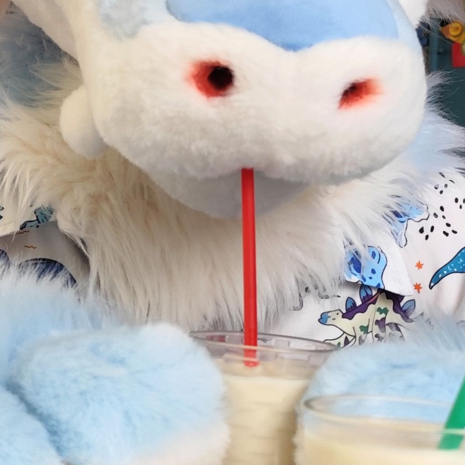 Photo of a person wearing a baby blue and off-white fursuit, cropped so that only the muzzle and part of the paws can be seen. The character looks like it's sipping some horchata through a straw while holding the glass with both hands. 