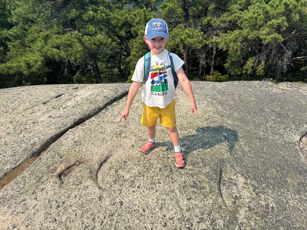 Four crescentic gouges (7-yr old pointing at three, and one in the far-right edge of image), which are moon-shaped chips removed from rock by subglacial erosion, preserved near the summit of Acadia Mountain, Acadia National Park, Maine. These gouges, which are types of chatter marks, point in the direction of the former glacial flow direction.