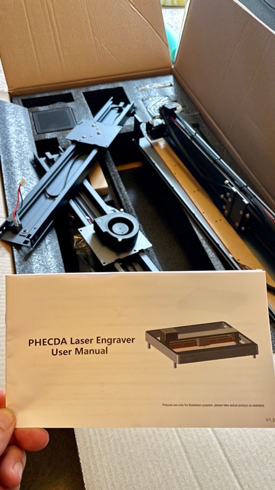 Laser cutter box with parts needing assembly and me holding manual up