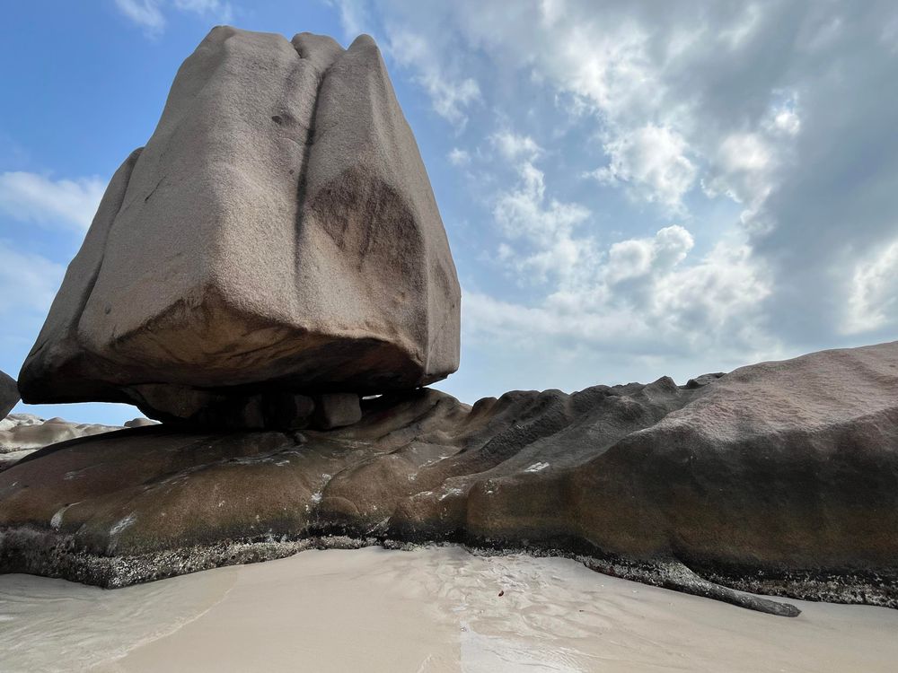 Niewiadomo w jaki sposób utrzymującą się  w równowadze wielka skała na pustej plaży tropikalnej 