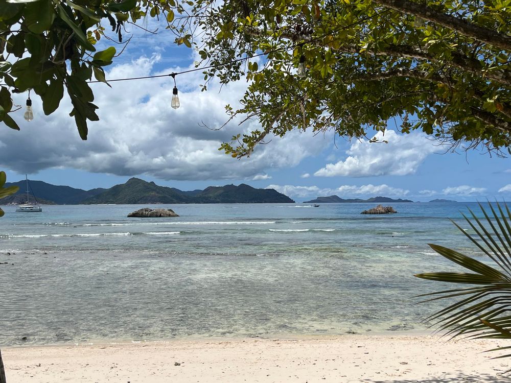 Piaszczysta plaża, ocean w niskiej fazie przypływu, w tle skały i kolejne tropikalne wyspy